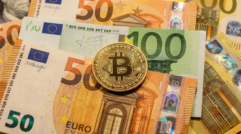 Una moneda dorada de Bitcoin apoyada sobre varios billetes de €.