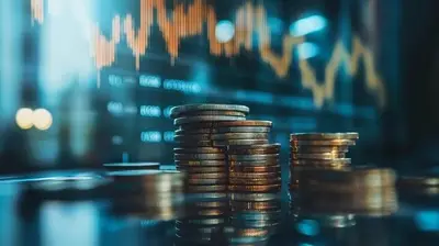 Pilas de monedas sobre una mesa, con un gráfico bursátil desenfocado de fondo.