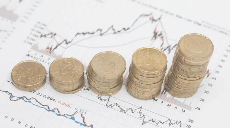 Pilas de monedas de € de altura creciente sobre gráficos bursátiles impresos.