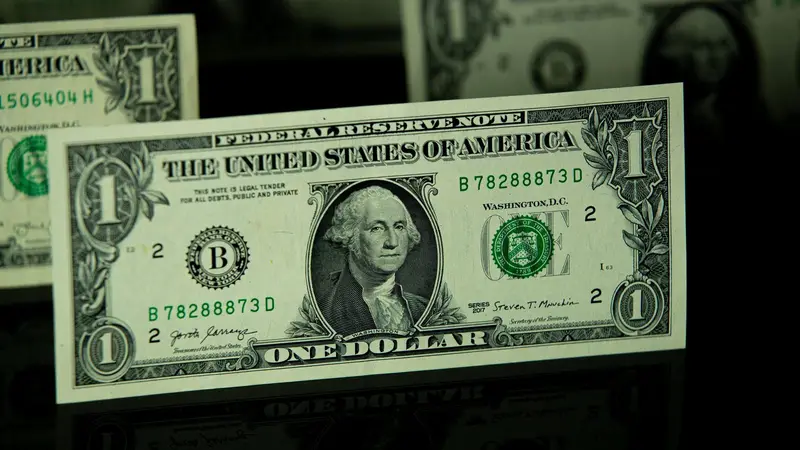 Un billete de $1 de la Reserva Federal con la inscripción Federal Reserve Note, iluminado sobre un fondo oscuro, con otros billetes desenfocados detrás