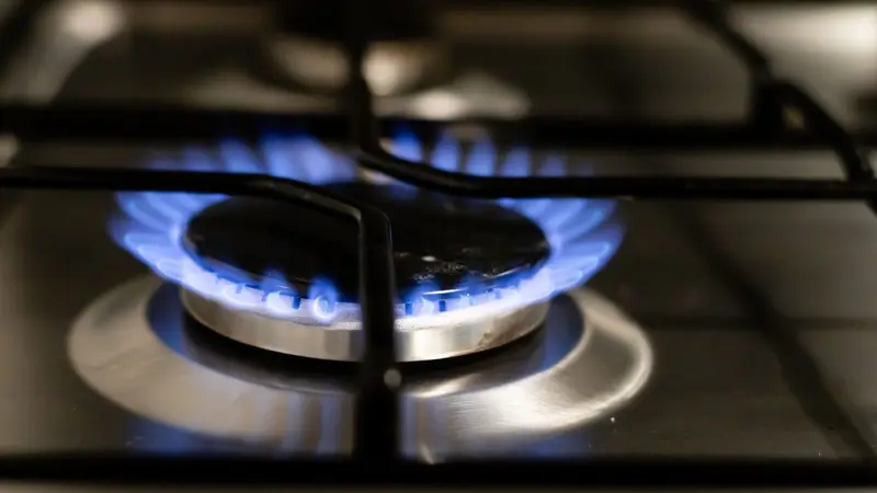 Primer plano de un fuego de gas con llama azul sobre una cocina de acero inoxidable, con las rejillas negras en primer plano