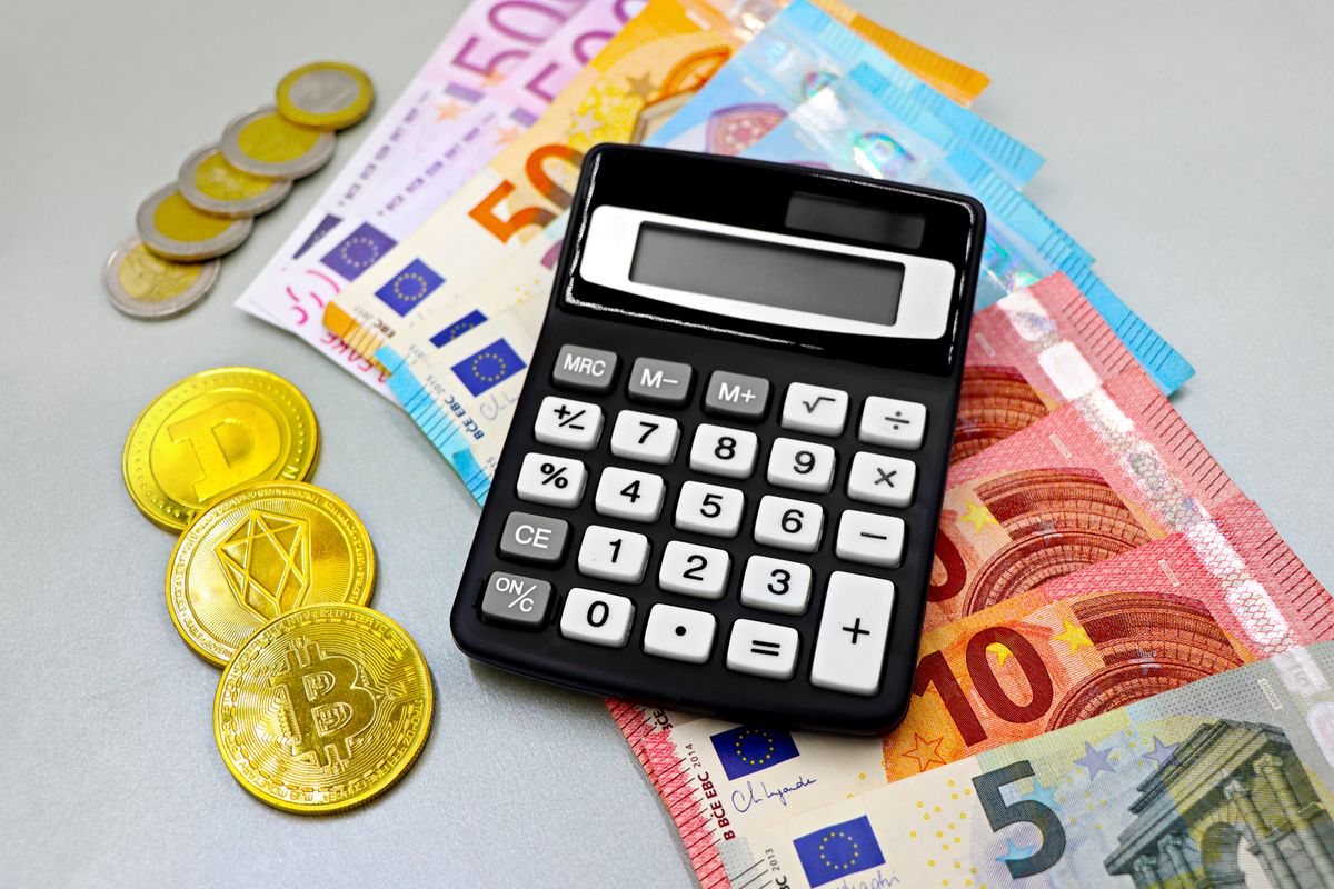 Una calculadora sobre billetes y monedas de €, junto a monedas de Bitcoin y otras criptomonedas.