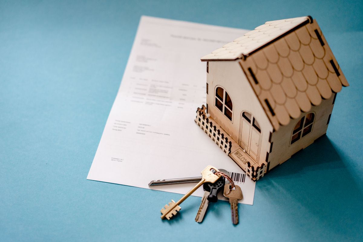 Una casa de madera en miniatura y un manojo de llaves sobre un contrato de vivienda.